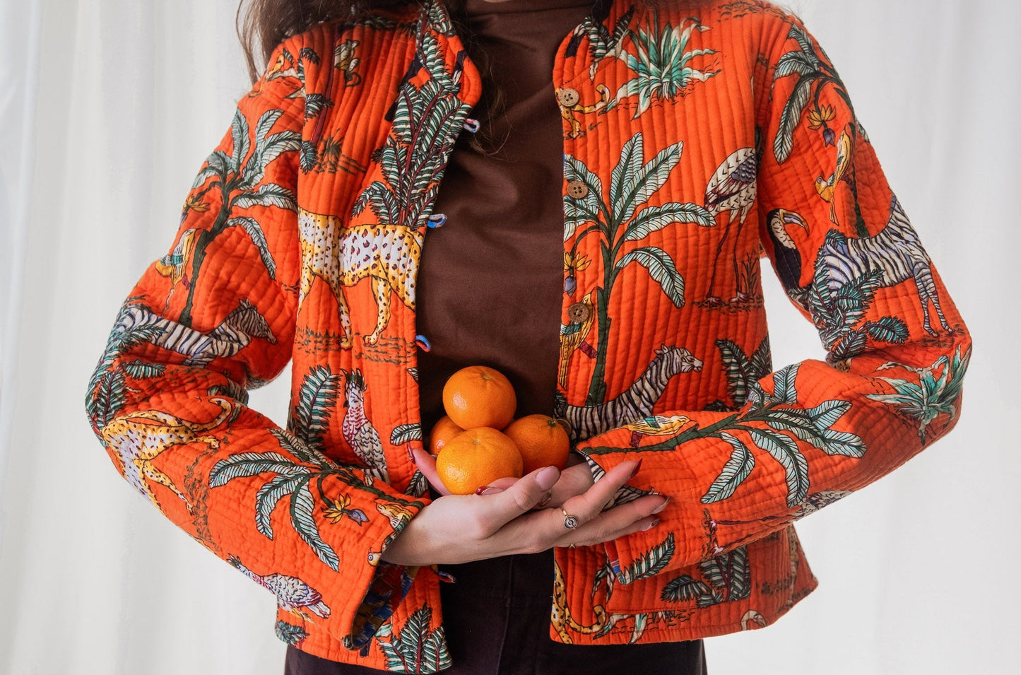 Person wearing an orange patterned jacket holding oranges against a white background