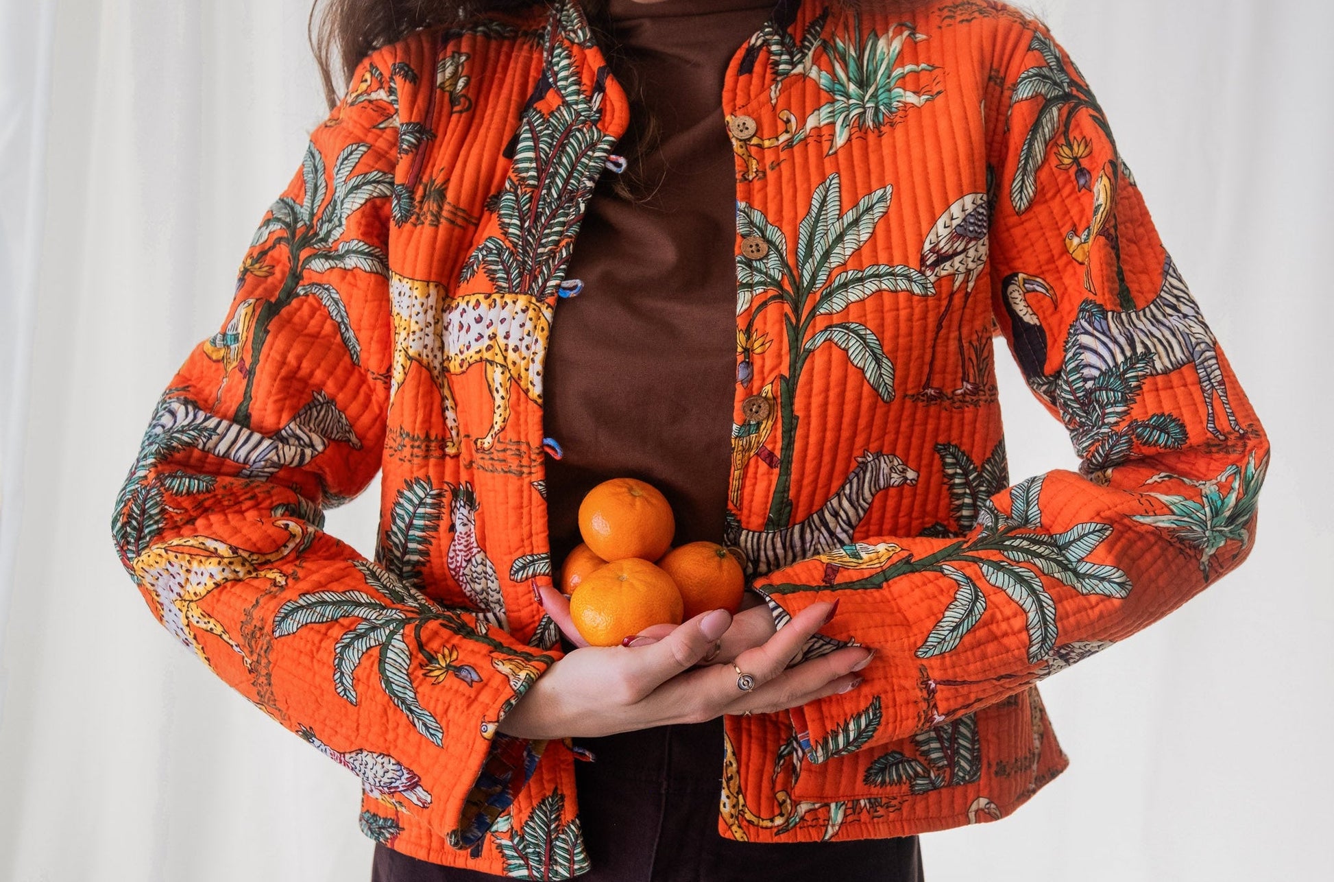 Person wearing an orange patterned jacket holding oranges against a white background