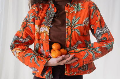 Person wearing an orange patterned jacket holding oranges against a white background